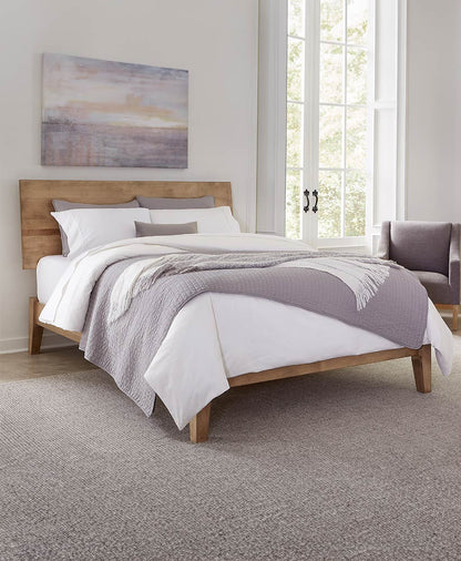 Bedroom with wooden bed frame, gray and white bedding, and a painting on the wall.