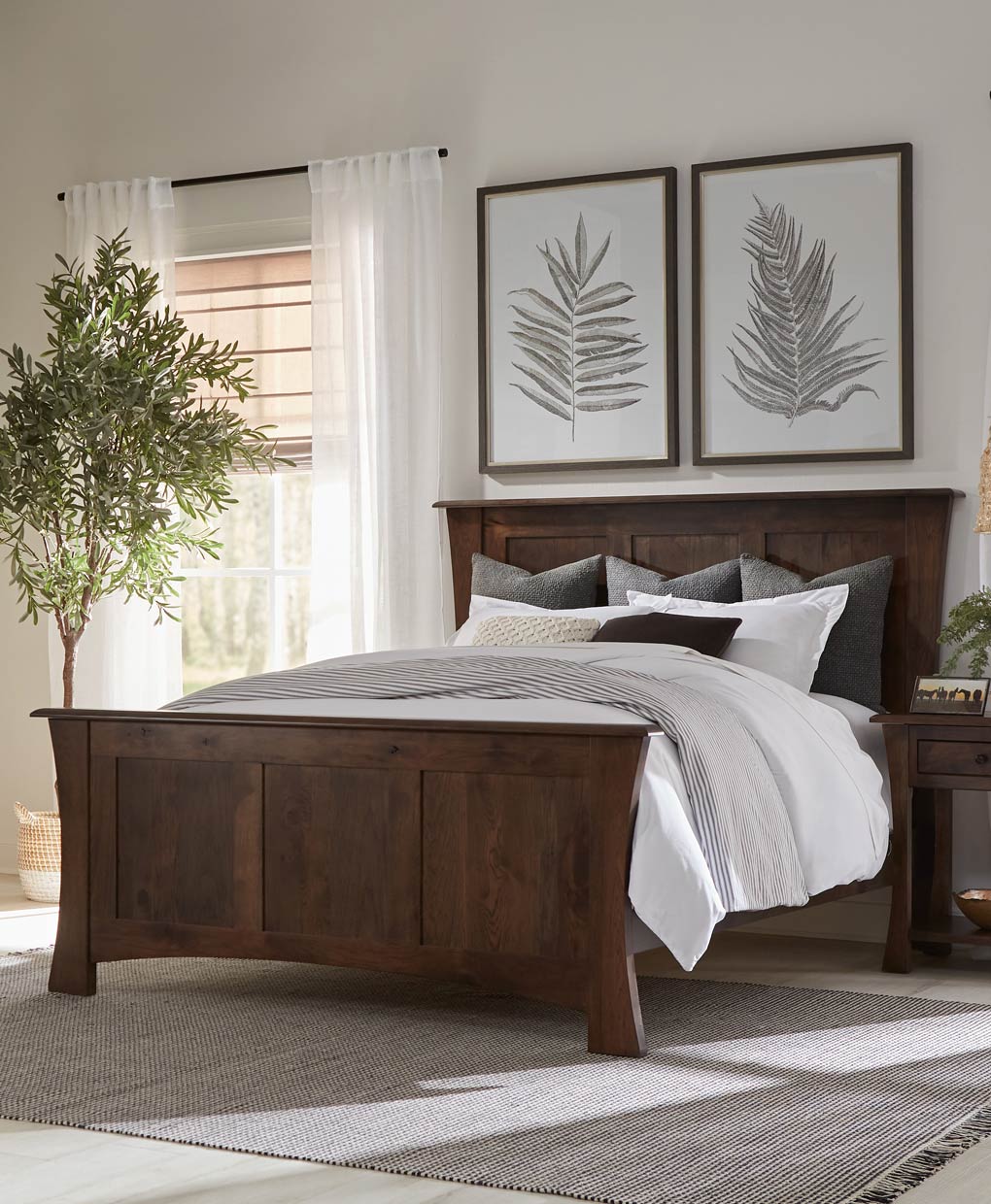 Wooden bed with white bedding in a bedroom setting with leaf artwork on the wall.